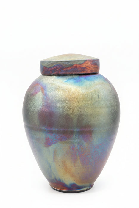 An iridescent ceramic urn with a matching lid, featuring a pearlescent finish that shifts between gold, green, blue, and purple, with reddish-orange marbling near the top, set against a dark gray background. Your urn will vary